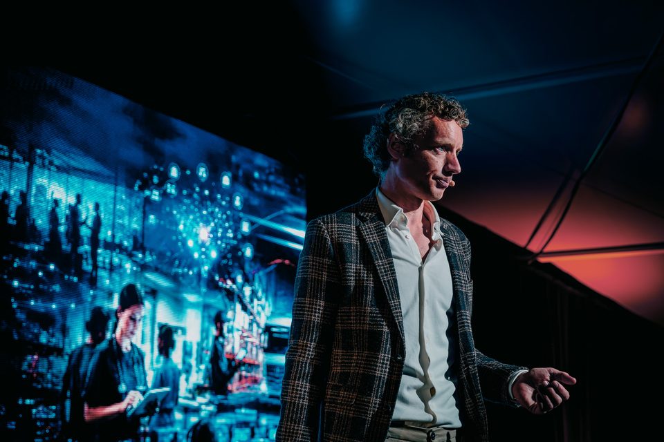 Laurens Waling op het podium van het Vlirdens WFM Congres, voor een groot scherm met een visualisatie van werk en skills